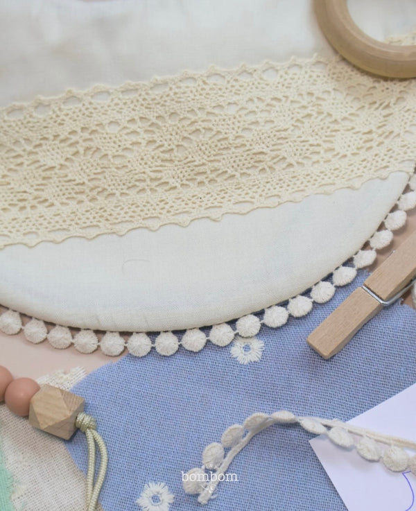 Detalle de encaje crema, borde de pompones y telas azules