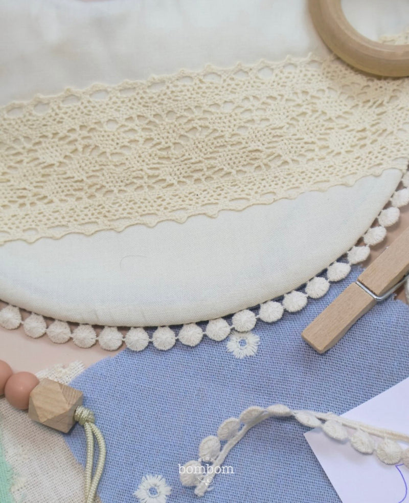 Detalle de encaje crema, borde de pompones y telas azules